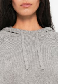 Camisola de capuz cinza claro, tricotada, com um acabamento texturizado, apresentando um cordão no decote e mangas raglan.