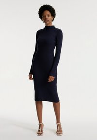 Navyblaues, geripptes Strickkleid mit hohem Kragen, langen Ärmeln und knielanger Länge. Es verfügt über eine taillierte Silhouette und einen weichen, strukturierten Stoff.