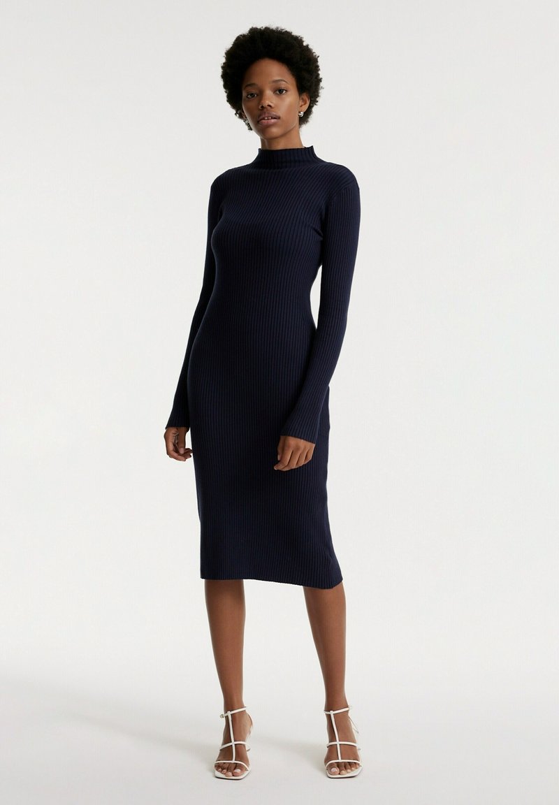 Navyblaues, geripptes Strickkleid mit hohem Kragen, langen Ärmeln und knielanger Länge. Es verfügt über eine taillierte Silhouette und einen weichen, strukturierten Stoff.