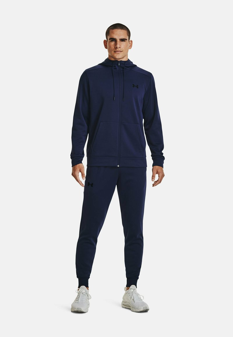 Granatowa bluza z kapturem na zamek i pasujące dresy wykonane z miękkiego materiału. Bluza ma sznurki do regulacji i kieszenie z przodu; dresy mają elastyczne mankiety.