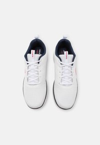 White athletic shoes with textured mesh upper, contrasting navy interior, six white laces, and red logo accents on the side and tongue.