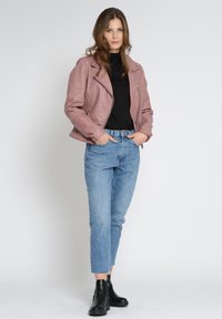 Veste en cuir rose de motard avec fermeture éclair argentée, col roulé noir, jean en denim taille haute bleu clair et bottines noires.