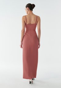 Rozā rozā krāsas grīdas garuma kleita ar plānām siksnām un piegulošu kroklu. Aizmugurē ir diskrēts rāvējslēdzējs un gluda faktūra.