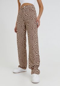 Bruine en crèmekleurige wijde broek met een geruit design. Gemaakt van lichte stof met een relaxte pasvorm, gedragen met witte sneakers.