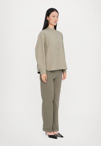 Khaki button-up shirt with a high collar, paired with matching trousers. Both have a relaxed fit and smooth texture. Black pointed heels.