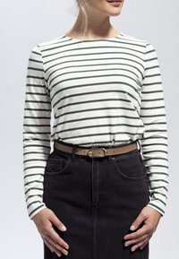 Långärmad vit och grönrandig skjorta i bomull, tillsammans med en högmidjad svart denimkjol och ett tanfärgat bälte med ett gyllene spänne.