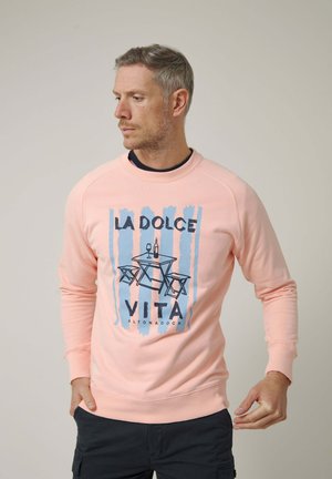 Hombre con sudadera de color rosa claro con rayas azules y un gráfico de una mesa, botella de vino y copas con el texto "La Dolce Vita".