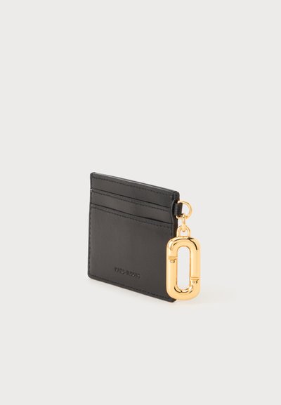 Porte-cartes en cuir noir avec deux emplacements pour cartes et un porte-clés ovale doré attaché sur le côté sur un fond clair uni.