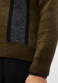 Καφέ πουλόβερ με γκρι κατακόρυφη ρίγα, υφασμάτινη πλέξη, ριμπ μανσέτες και στρίφωμα. Διαθέτει διακριτικό λογότυπο κοντά στο κάτω μέρος. Μαλακό υλικό από μείγμα μ�αλλιού.