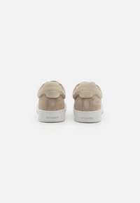 Beige semskinnssneakers med en glatt lyse beige lærrygg, avrundet hæl og hvite gummisåler; har «BOGNER»-merket på baksiden.
