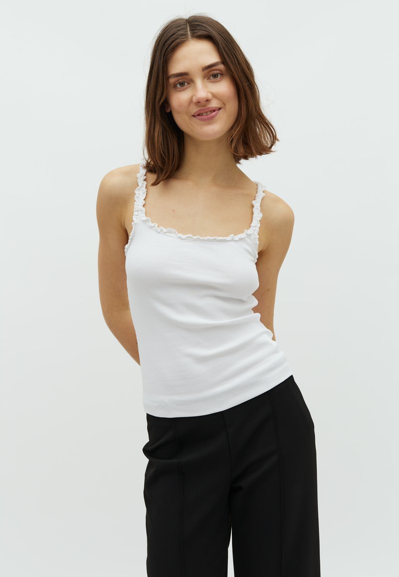 Witte geribbelde tanktop met rimpel-laceafwerking langs de halslijn en schouderbanden, gedragen met zwarte losse broeken. Glad textuur en slanke pasvorm.