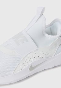 White athletic shoe with a breathable mesh upper, elastic strap, perforated detailing, and a textured sole featuring a subtle logo.
