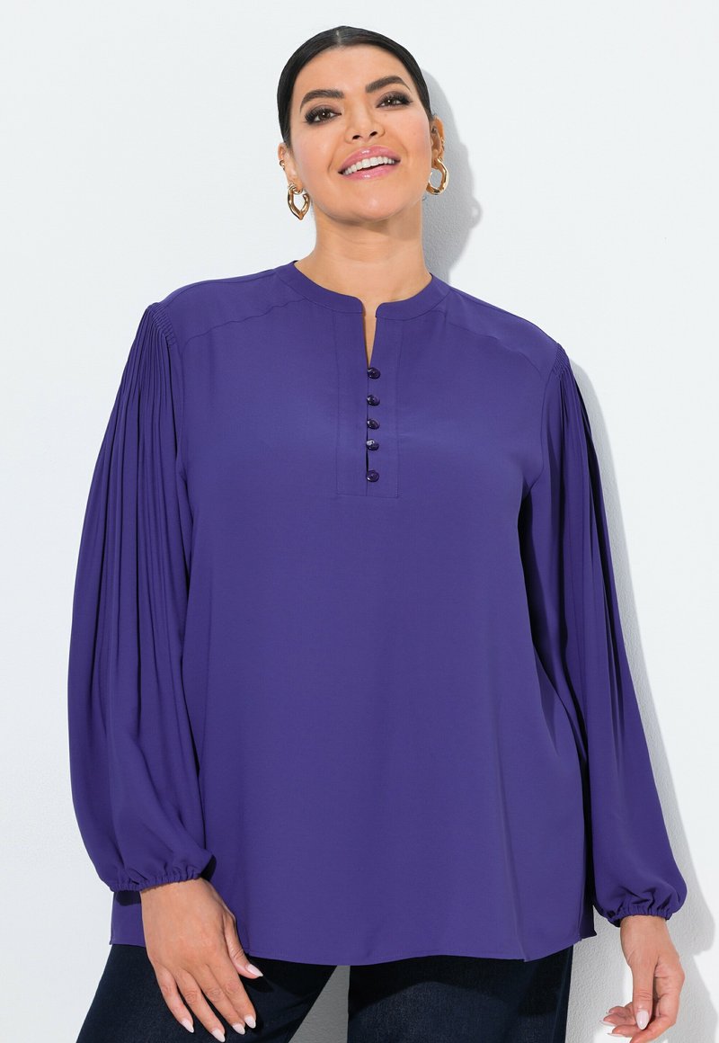 Blusa viola con scollo rotondo, chiusura a bottoni e maniche lunghe arricciate. Realizzata in tessuto morbido con una vestibilità comoda.