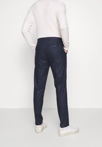 Pantaloni a scacchi blu navy con vestibilità su misura, dotati di cintura e tasche laterali. Abbinati a un top in maglia leggera e sneakers bianche.