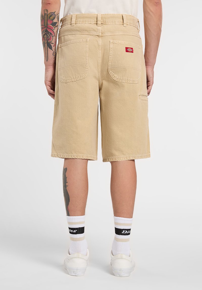 Pantalones cortos cargo beige con un diseño de pierna recta, fabricados con una tela resistente. Cuentan con dos bolsillos traseros y una etiqueta de marca roja en el bolsillo derecho.