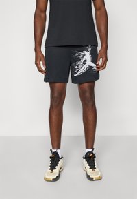 Sorte atletiske shorts i tekstureret mesh stof med et kontrastfyldt hvidt grafisk design på venstre side. Sammen med lyse sneakers.