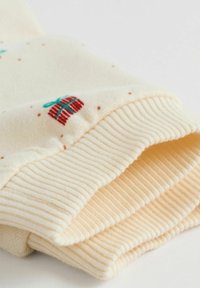 Gebreide crèmekleurige trui manchet met een geweven rood presentontwerp en een turkooise strik. Geribbelde textuur aan de manchet met kleine bruine stippen doorheen.