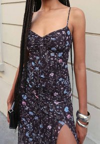 Czarna sukienka w kwiatowy wzór z cienkimi ramiączkami, marszczonym zdobieniem i wysokim rozcięciem. Ozdobiona niebieskimi i różowymi kwiatami, o dopasowanym kroju i gładkim materiale.