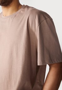 Korte mouwen, ronde hals t-shirt in een lichtbruine kleur. Gemaakt van een gladde, zachte stof met een relaxte pasvorm en minimale stikseldetails.