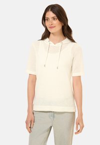Haut à manches courtes avec capuche en tissu blanc texturé avec un design en maille, présentant un cordon de serrage et une coupe décontractée.
