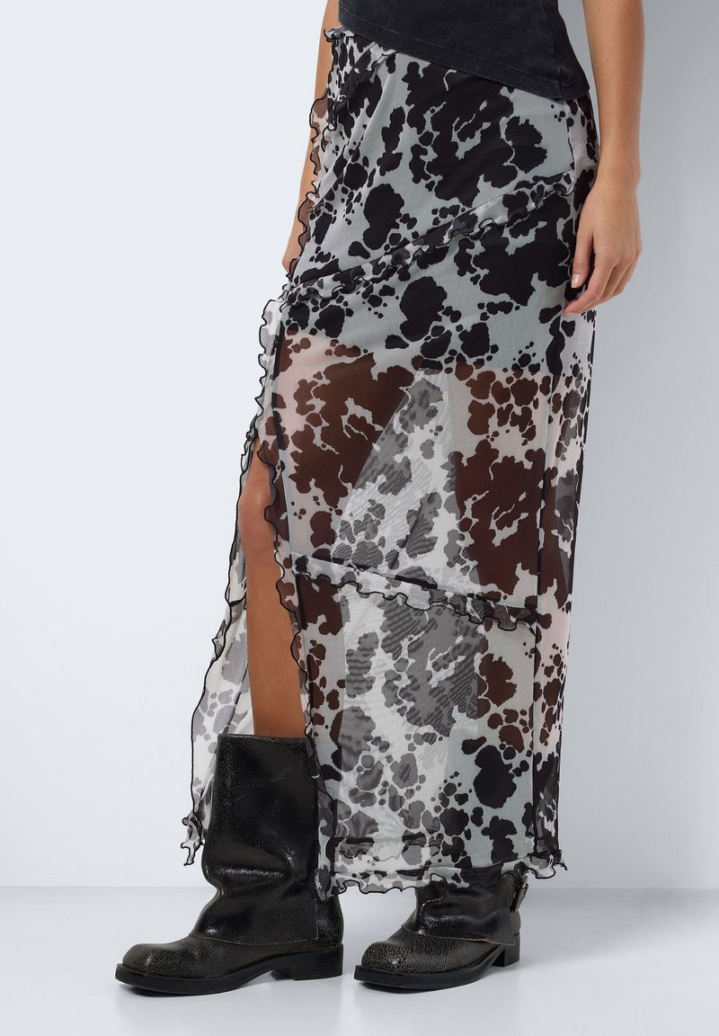 Jupe transparente noire et grise avec un motif éclaboussé, des bords volantés et une fente haute jusqu'à la cuisse, associée à des bottes noires texturées mi-mollet.