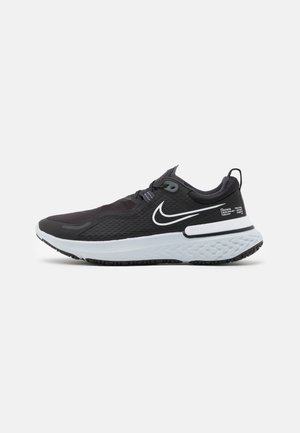 Schwarz-weißer Nike-Laufschuh mit strukturiertem Obermaterial, gepolsterter weißer Sohle und Zuglasche an der Ferse, seitlich auf grauem Hintergrund gezeigt.