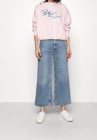 Ljusrosa hoodie med marinblå text, i kombination med vida, blekta blå denimjeans och vita sneakers. Mjuk tygkvalitet, avslappnad passform.