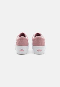 Vaaleanpunaiset tekstiili-tossut, joissa on valkoinen kumipohja ja yksityiskohtia. Takana on logo, jossa lukee "VANS OFF THE WALL." Matala profiilimuotoilu.