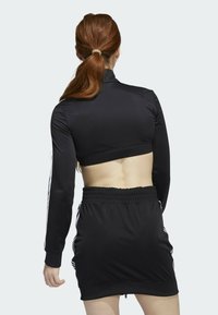 Black athletic top with long sleeves and cropped design, paired with a black skirt featuring an elastic waistband and white side stripes.