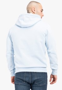 Felpa di un blu chiaro con cappuccio regolabile, texture morbida, tasca a marsupio e polsini a costine. Indossata con jeans in denim scuro.