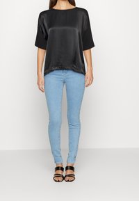Top corto in satin nero con scollo rotondo, abbinato a jeans skinny azzurri e sandali neri con cinturini.