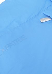 Giacca azzurro chiaro con una finitura liscia e opaca. Presenta una clip in metallo argentato e un logo impressato. Il design include dettagli di cucitura sottili.