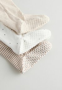 Trzy pary skarpetek: jasnobeżowe prążkowane, białe w szare kropki oraz beżowe w paski. Wszystkie mają teksturowane, antypoślizgowe podeszwy.