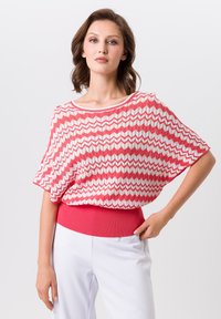 Roze en witte top met zigzagpatroon, heeft een brede halslijn en korte mouwen, en is voorzien van een effen roze geribbelde tailleband.