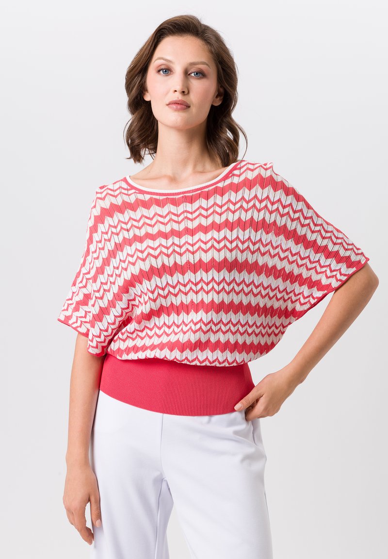 Roze en witte top met zigzagpatroon, heeft een brede halslijn en korte mouwen, en is voorzien van een effen roze geribbelde tailleband.