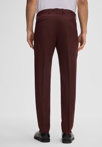 Bordeaux kleurige broek met een gladde textuur, rechte voorkant en twee achterzakken. Gecombineerd met een eenvoudig t-shirt en zwarte schoenen.