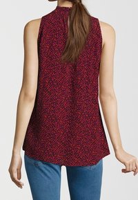 Woman wearing sleeveless red and purple leopard print top paired with blue jeans, shown from the back.