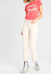 Punainen lyhythihainen T-paita valkoisella painatuksella, yhdistettynä off-white suoraan leikattuihin farkkuihin ja kiiltävän hopeisiin nilkkureihin, joissa on korkeat kapea korko.