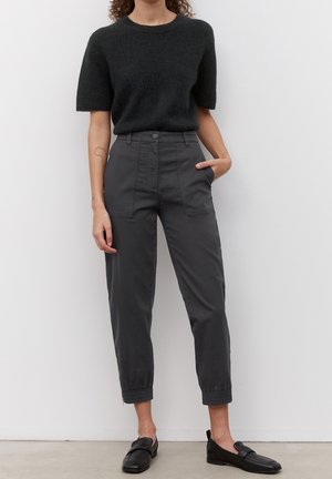 Maglione corto a maniche corte in maglia nera e pelosa abbinato a pantaloni gessati grigio scuro a vita alta con tasche frontali e polsini elasticizzati. Mocassini neri.