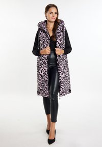 Padded Weste in Pink mit schwarzem Leopardenmuster, ausgestattet mit Kapuze, Reißverschluss und seitlichen Taschen, kombiniert mit schwarzen Leggings und High Heels.