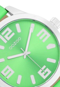 Green analog wristwatch with a matte finish, silver hour markers, and hands, featuring a silver bezel and a green strap.