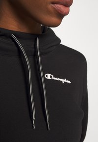 Sudadera con capucha negra y logo blanco de "Champion", con cordones en contraste blanco y negro y un tejido texturizado.