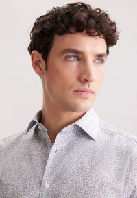 Camicia a maniche lunghe con stampa floreale in azzurro chiaro e bianco, caratterizzata da un colletto alla francese, tessuto morbido e dettagliati motivi sparsi.
