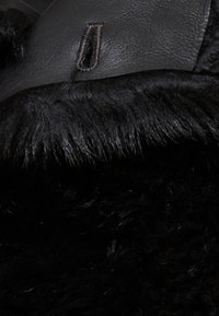 Sort kunstpelsstof med et glat læderrem, der har en syet løbdetail. Blød tekstur med rig dybde og glans.