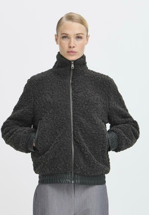 Schwarze, flauschige Fleece-Jacke mit hohem Kragen, Reißverschluss vorne und gerippten Bündchen sowie Saum. Verfügt über zwei seitliche Taschen.