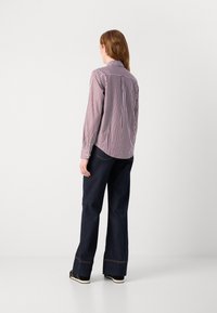 Camicia a righe rossa e bianca, con colletto e maniche lunghe. Abbinata a pantaloni larghi in denim scuro e scarpe nere.