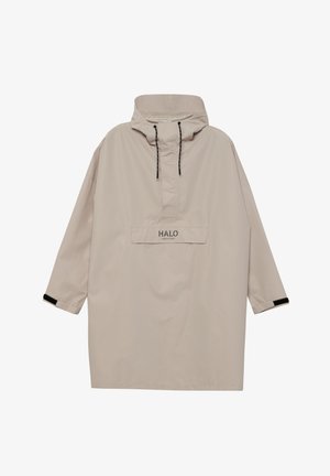 Lyst beige anorak med høj hals, sorte snore, forlomme og kontrastfyldte sorte detaljer ved manchetterne. Glat, vandafvisende stof.