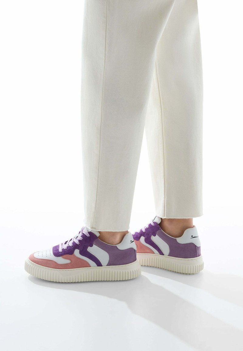 Les baskets présentent une base en cuir blanc avec des panneaux en suède violet et rose, une semelle en caoutchouc texturée et des lacets ronds. Design minimaliste avec des touches d'accent.