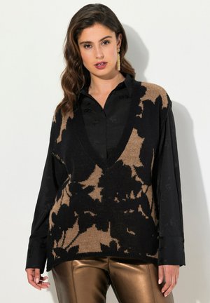 Strikket vest med dyb V-hals, der har en sort bundfarve og store brune blomster mønstre, lagd over en sort skjorte med subtil struktur.