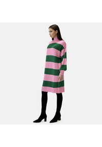 Vestido de punto con amplias rayas rosas y verdes, cuello alto y mangas largas; combinado con mallas negras y botas de tobillo.